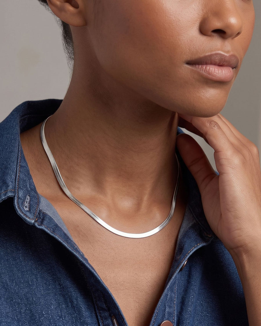 Model Image - Stainless steel herringbone chain necklace with a smooth, flat profile resting at the neckline worn on model