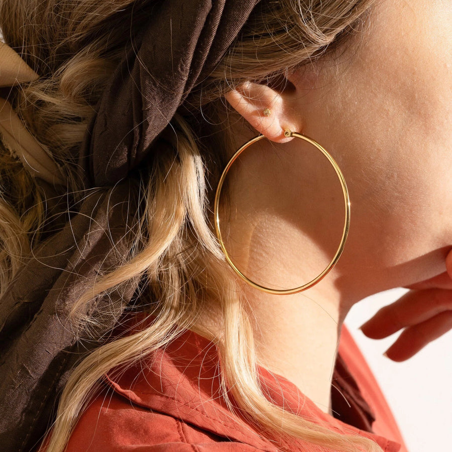 model image- Close-up of a person wearing a gold hoop earring with a blurred background