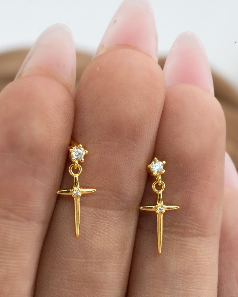 Model Image - Cross drop studs with a delicate dangling cross design shown against the fingers worn on model
