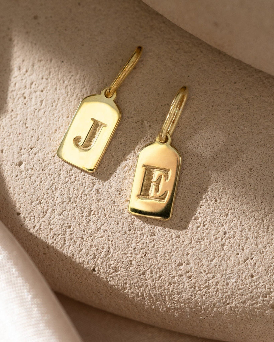 Detail Image - 14K gold initial tag charms with engraved letters J and E on a textured surface