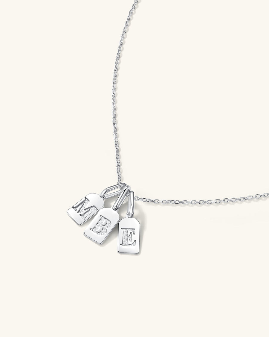  Three rhodium initial tag charms with engraved letters on a delicate necklace chain worn on model